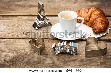 Cup of black coffee with croissant and heart decoration on rustic wooden background. romantic french breakfast with deco symbol of paris eiffel tower