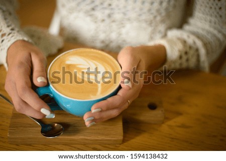 blue cup with coffee in hands of girl, cappuccino on stand
