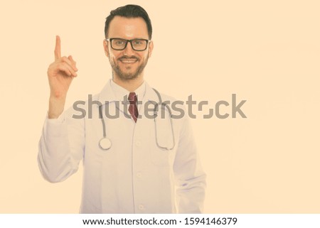 Studio shot of young happy man doctor smiling while pointing finger up
