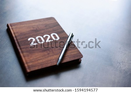 View on personal book calendar with 2020 year on cover, lay on table in light. Wooden pattern. Plan for new year.