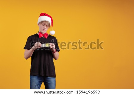 Young guy in a red Santa Claus hat holds in his hands banknotes, money and posing on a yellow background