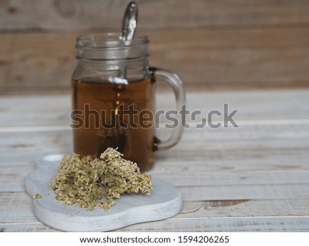 Tea in a glass and dried yarrow flowers for use in traditional medicine on a white wooden ancient table.