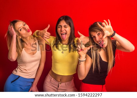 Stock studio photo of three girls posing with funny expression in front of a red wall