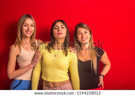 Stock studio photo of three girls of different appearance standing in front of a red wall