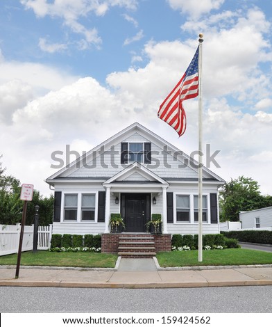 Suburban Cottage Style Bungalow Home with American Flag Landscaped front yard residential neighborhood USA Blue sky Clouds