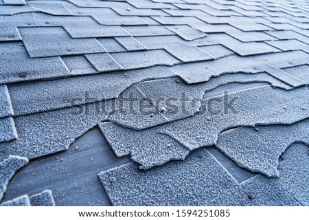 Close up view on Asphalt Roofing Shingles roof damage covered with frost.