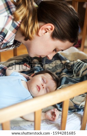Young woman kissing her sleeping baby in bed at home. Family, maternity, child care concept.