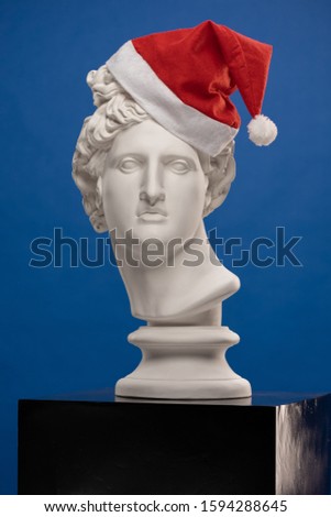 Statue of a bust of Apollo's head  in a red cap of Santa Claus on a blue background