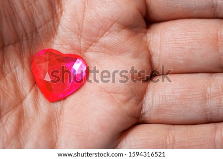 Small glass red heart in a male palm. The subjects of medicine, sociology, health preservation and declaration of love. Macro.