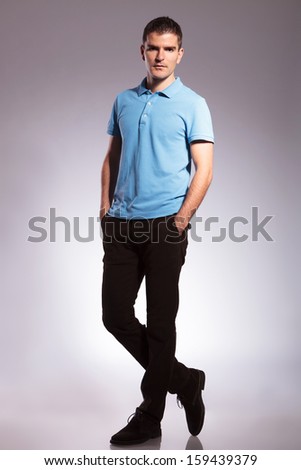 full length picture of a young casual man standing with his hands in his pockets and looking into the camera. on gray background