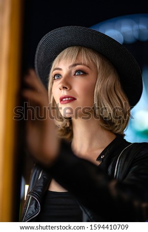 The World Of Magic. Beautiful mysterious woman exploring night city alone. Checking the route on the lightbox map in the city. Close up portrait of stylish blonde girl in hat looking aside
