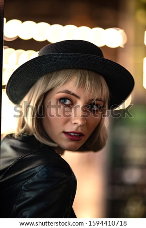 Love Every Moment. Beautiful mysterious woman exploring night city alone. Copy space in lower right part. Close up portrait of stylish blonde girl in hat looking away while having fun outdoor.