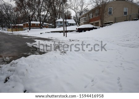 Snow on the ground and some footprints in it. A neighborhood of houses and a car. Picture taken in Kansas City, Missouri.