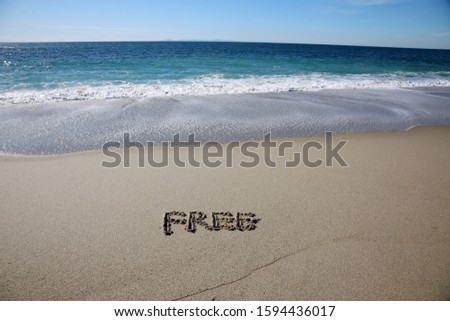 Free written in beach sand. The world FREE written in beach sand with blue pacific ocean water and tide in the background. Laguna Beach California. Vacation spot for world travelers. 