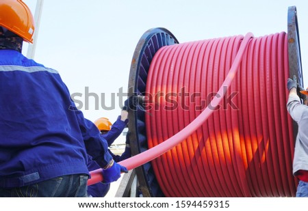 Workers pulling high voltage cable line or large electric cable from big steel cable drum in chemical plants, power plants, oil & gas industry or onshore. Royalty-Free Stock Photo #1594459315