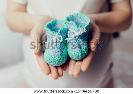 A pregnant woman is holding knitted booties on outstretched arms against the background of her belly. Great time to wait for the baby. Close-up photo of a pregnant belly.