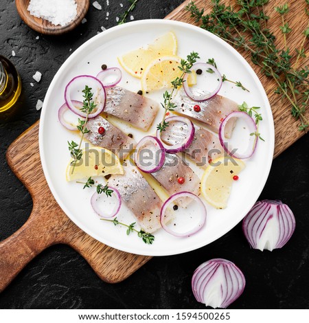Salted herring with spices, lemon and red  onion rings on black stone background . Marinated sliced fish. top view Royalty-Free Stock Photo #1594500265