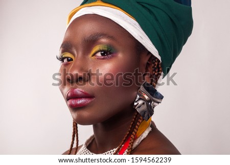 Studio portrait of African young woman with vibrant makeup of yellow and green colors. Colorful ethnic headwrap. White background. Fashion style.