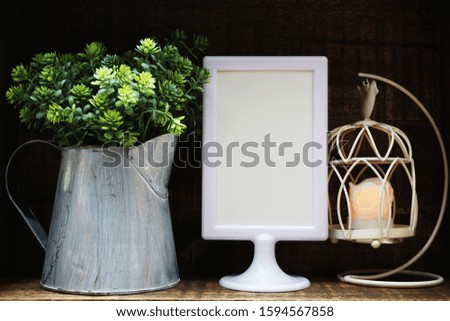 Blank Display frame stand with bird cage lantern and artificial plant on wooden background