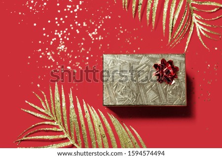 Christmas present in a golden box and gold decorations on red background. Valentines day gift. Top view. Copy space.
