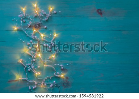 Christmas lights decoration on wood texture blue background. Glowing garland on vintage painted backdrop. Space for text, top view.