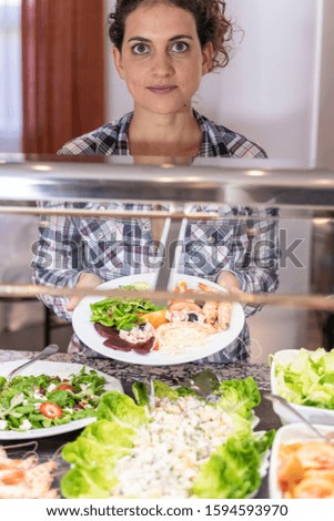 Stock vertical photo of a girl showing a plate of salad with prawns in a self-service restaurant