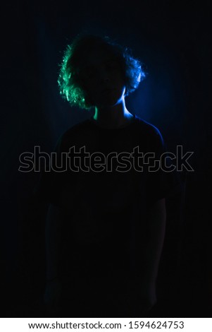 blue-green silhouette of a girl with curls on a black studio background. in the light of colored lamps.
