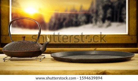 Wooden window sill and winter landscape of forest and orange sky with sunset.Kettle on board and free space for your decoration.Hot drink of tea, coffee or mulled.View of forest with frost and ice. 