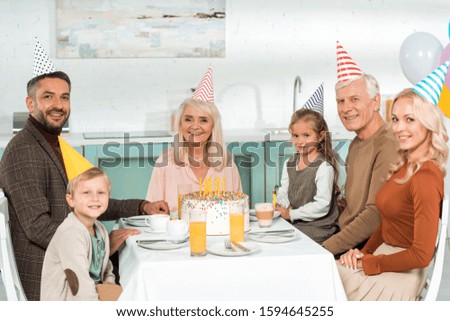 happy family looking at camera while sitting near kitchen table with birthday cake