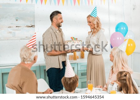 smiling man presenting birthday cake to happy wife while all family sitting at kitchen table