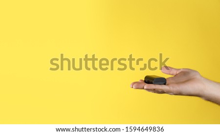 Male holds in the palm of hand black accumulator for dslr on a yellow background. Rechargeable lithium ion battery for digital camera. Copy space.