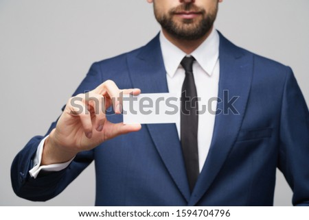 studio photo of young handsome businessman wearing suit holding business card