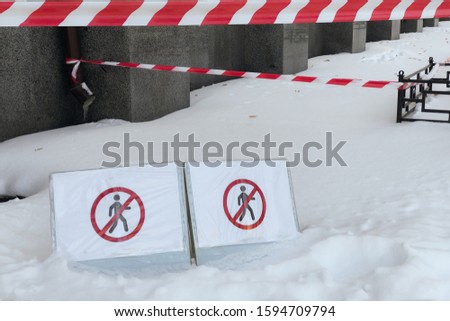 the place under the house is closed for pedestrians because of the danger of ice and snow fall from the roof. Danger of falling ice and snow during winter. snow fall fenced in red-white ribbon
