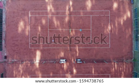 Tennis court seen from above in vertical shot with two players playing a match.