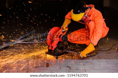 Asian man worker wearing yellow protective mask and fire protection gloves with personal protection equipment sitting cutting steel by fiber circular saw machine in factory.