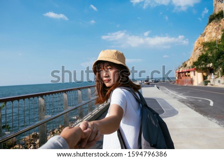 Girl in light brown hat and white t-shirt walk along the fence at the road side next to the sea with blue sky.