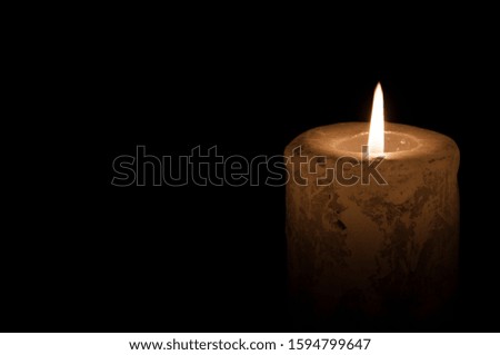 A large candle burns in the dark. On a wooden background.