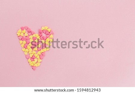 heart of pink and yellow confetti confectionery on a pink background copy space.