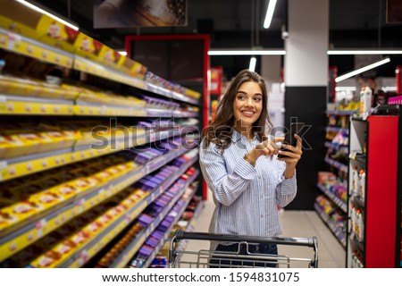 Woman do shopping check to buy list in phone. Women shopping in supermarket. Pretty young woman buying groceries in a supermarket/mall/grocery store.