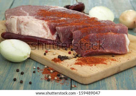 Raw meat on a cutting board with onion and chili pepper.