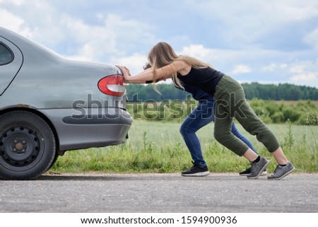 Two girls pushing their car which has run out of petrol along a country road in summer day Royalty-Free Stock Photo #1594900936