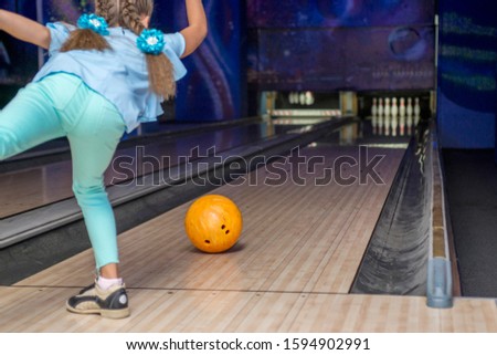 Young girl throwing a ball in bowling club. Kid is playing bowling. View from behind.