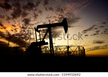 Silhouette of crude oil pump in the oilfield at cloudy sunset