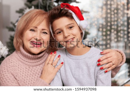 Happy young boy in Santa Claus hat smiling to the camera with his lovely grandmother. Family Christmas concept