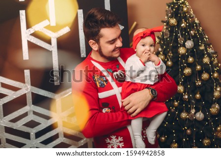 Handsome man in a red sweater. Family near christmas tree. Little girl in a cute dress