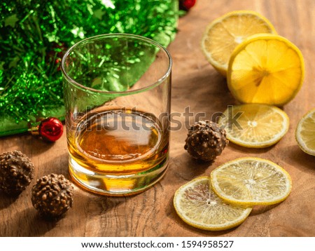 Cognac in a glass, lemon and chocolate on a wooden table. Christmas decoration on the background.