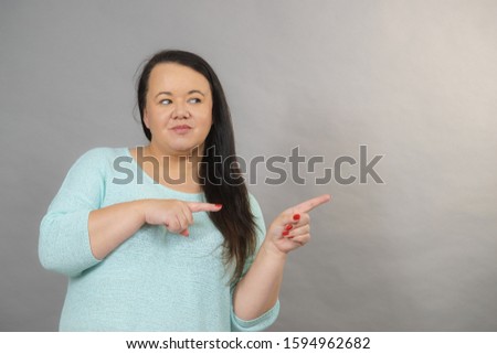 Plus size adult woman with dark hair pointing at copy space on gray background, advertising something.