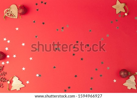 Christmas festive red background with a place for text on which glittering stars and wooden decorative ornaments and Christmas toys lie