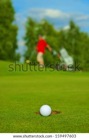 Golf, ball lying on the green next to hole, in the background goes golfer