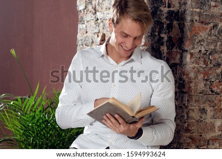 A young Smiling man in a white shirt reading a book. Business literature for self-development. Student or young businessman.